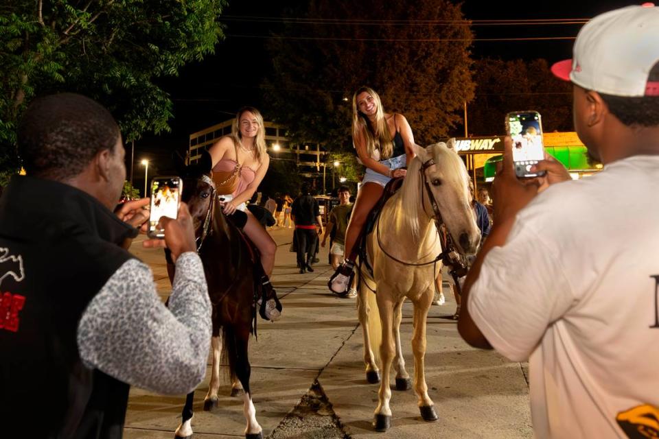 Stephen Harmon, left, and Brandon Mack photograph Faith McElwaine and Krista Kobi on Harmon’s horses in Columbia’s Five Points on Wednesday, May 10, 2024. Harmon charges students for rides and photo-ops.