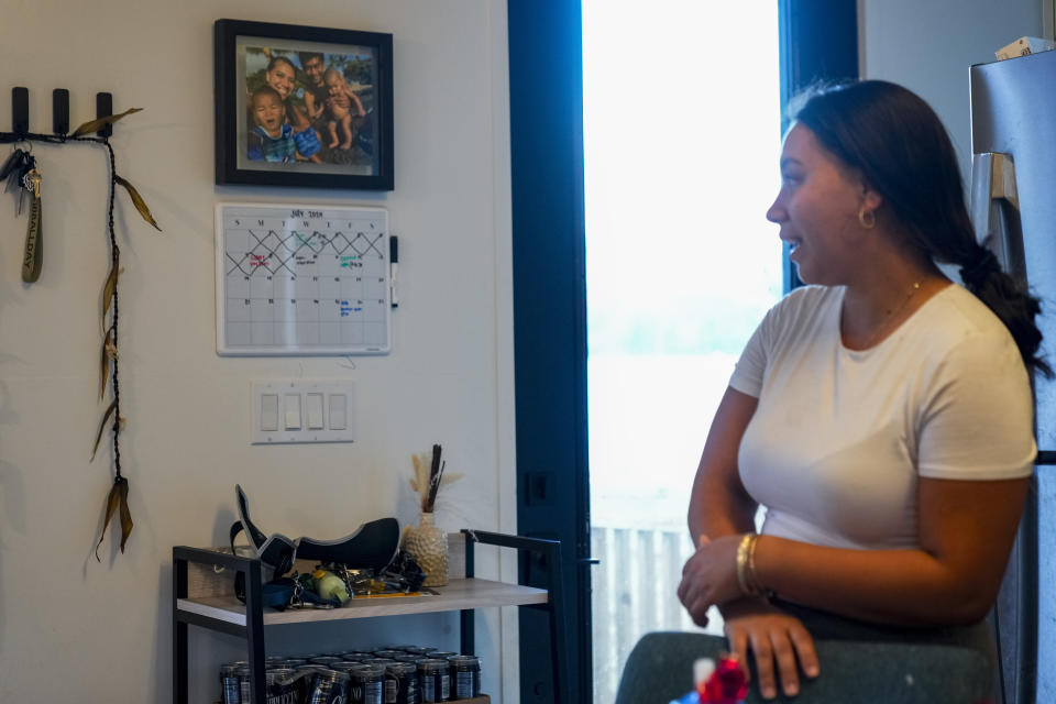 Josephine Fraser, 22, who was born and raised in Lahaina, looks at a hung family photo the Council for Native Hawaiian Advancement printed for them in their new home at Ke Ao Maluhia at the Maui Lani housing development, Wednesday, July 10, 2024, in Kahului, Hawaii. The family has moved 10 times over the past 11 months after being displaced by the 2023 wildfire and are the first to move into the modular home community being built for those affected. (AP Photo/Lindsey Wasson)