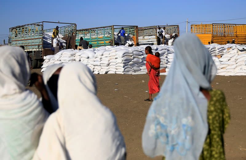 Women watch as workers off-load sacks of food from trucks to deliver it to Ethiopian refugees fleeing from the ongoing fighting in Tigray region, at the Fashaga camp, on the Sudan-Ethiopia border, in Kassala state