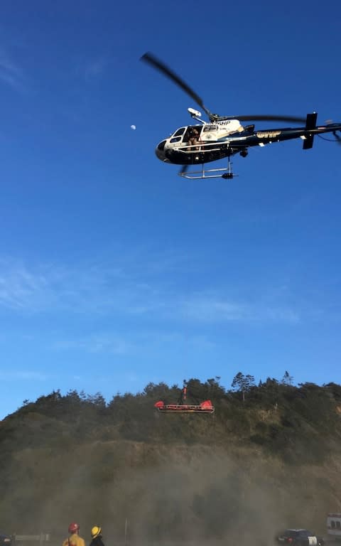 a helicopter hovering over the scene where a vehicle plunged off a cliff - Credit: California Highway Patrol 