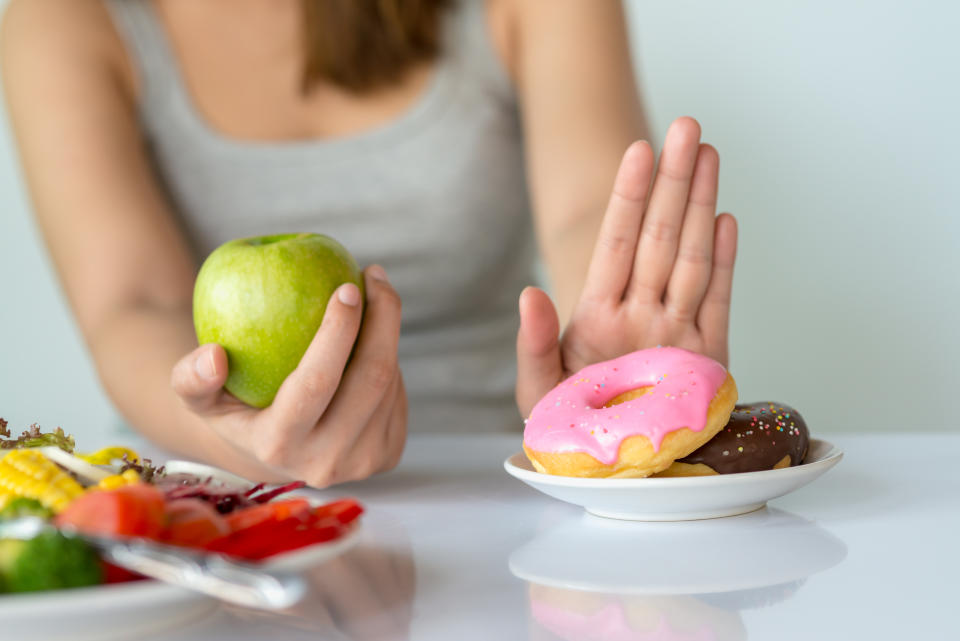 Dieting or good health concept. Young woman rejecting Junk food or unhealthy food such as donut or dessert and choosing healthy food such as fresh fruit or vegetable.