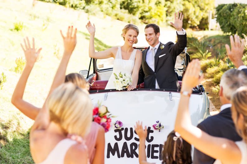 Newlywed couple in the back of a car decorated with a Just Married banner.