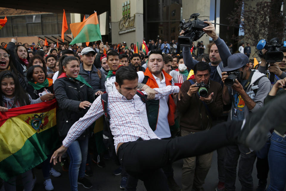 Supporters of opposition presidential candidate Carlos Mesa, a former president, hold back a fellow supporter trying to kick supporters of Bolivian President Evo Morales, who is running for a fourth term, as rival groups gather outside the Supreme Electoral Court where election ballots are being counted in La Paz, Bolivia, Monday, Oct. 21, 2019. A sudden halt in release of presidential election returns led to confusion and protests in Bolivia on Monday as opponents suggested officials were trying to help Morales avoid a risky runoff. (AP Photo/Jorge Saenz)