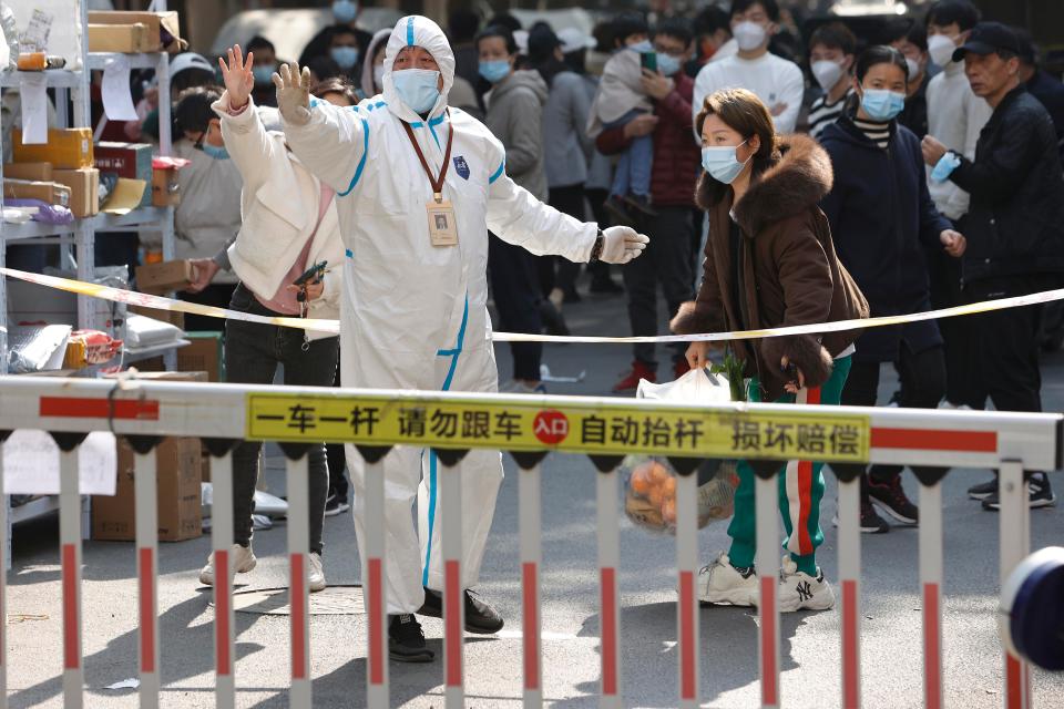 A volunteer wearing PPE raises their hand at a residential gate.