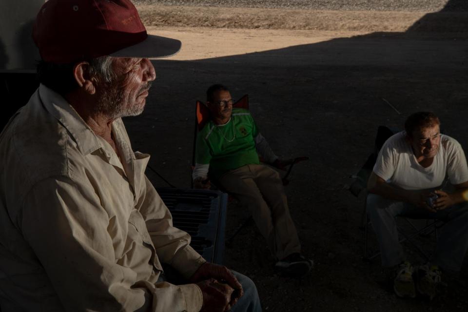 Three farmworkers rest in the shade of a bridge