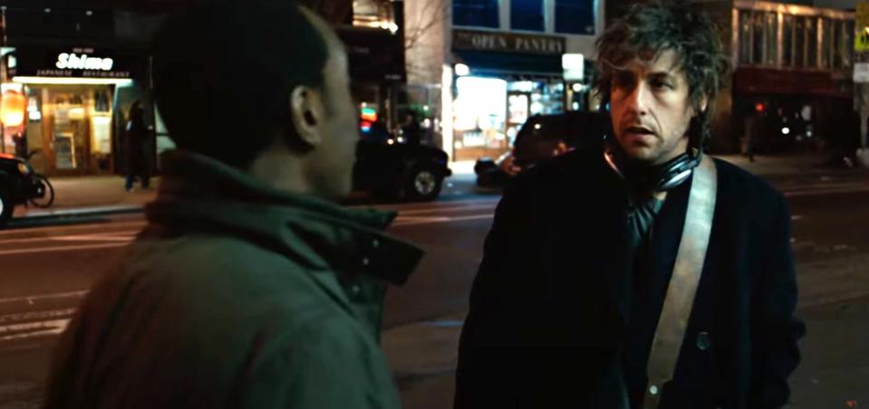 Don Cheadle and Adam Sandler in a scene, standing on a street at night, engaged in conversation