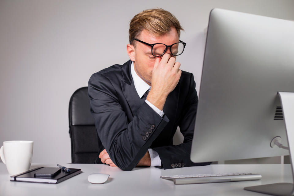 Frustrated mean wearing suit holding face in front of computer.