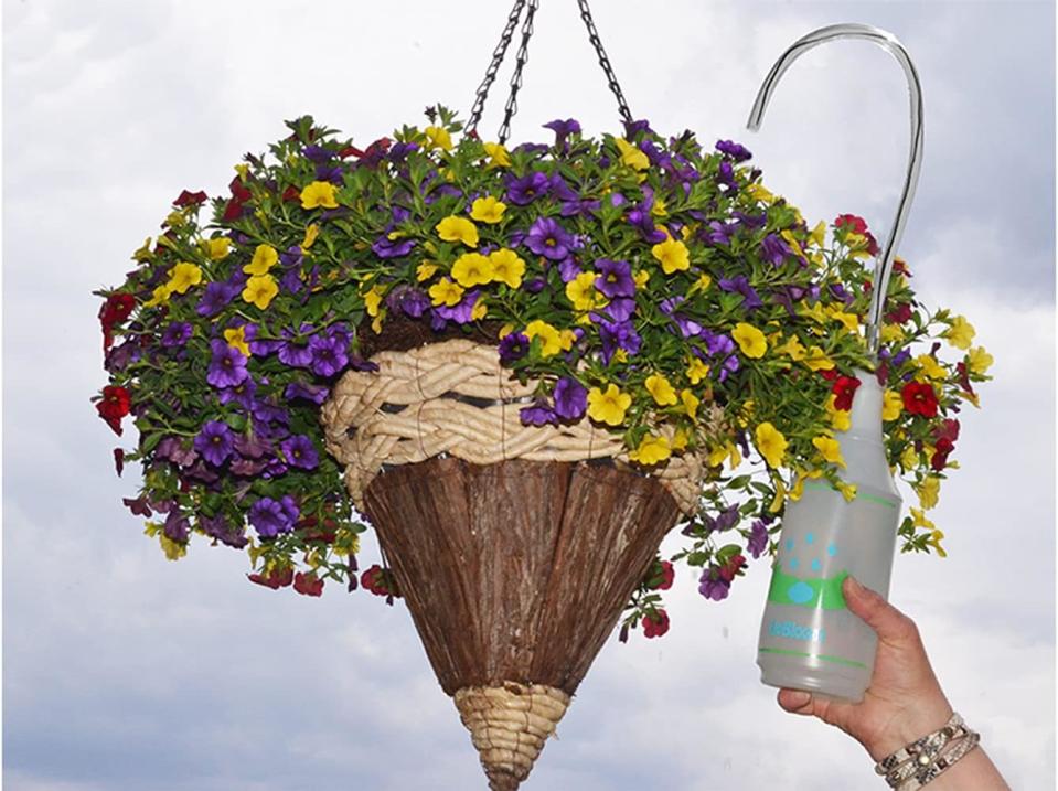 a hand using the UpBloom plant water bottle to water a hanging planter of flowers