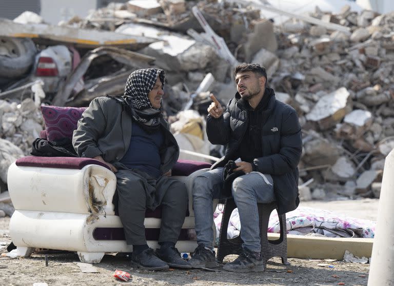 Dos damnificados conversan frente a los escombros de un bloque de departamentos en Antakya, Turquía