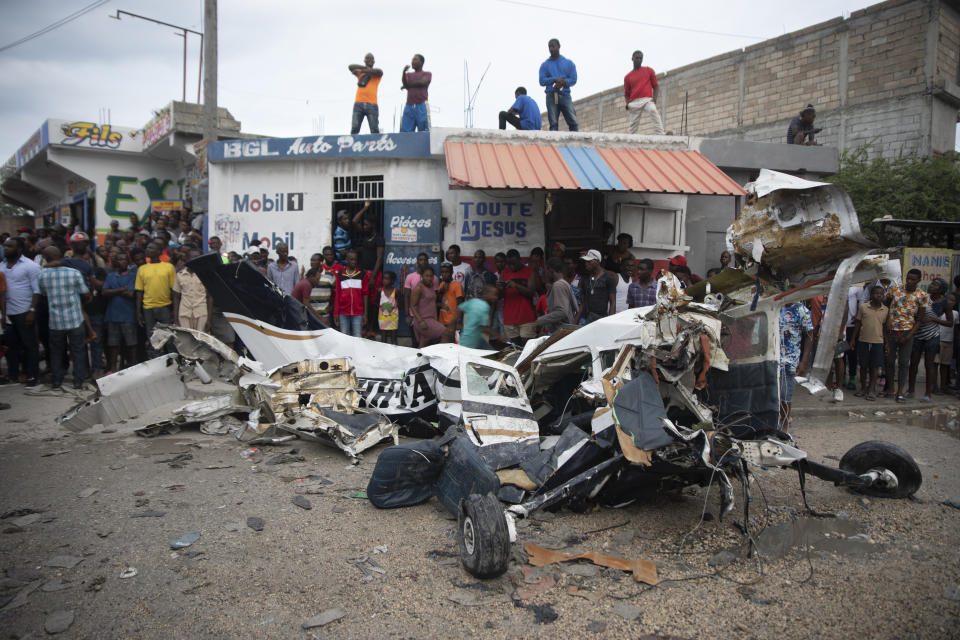 Onlookers mill around the wreckage of a small plane that crashed in the community of Carrefour, Port-au-Prince, Haiti, Wednesday, April 20, 2022. Police report that the plane was headed to the southern coastal city of Jacmel when it tried to land in Carrefour and that at least 5 people died in the accident. (AP Photo/Odelyn Joseph)