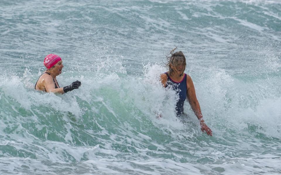 Two people attempt to go for an early morning swim in heavy waves at Gyllyngvase Beach in Falmouth, Cornwall