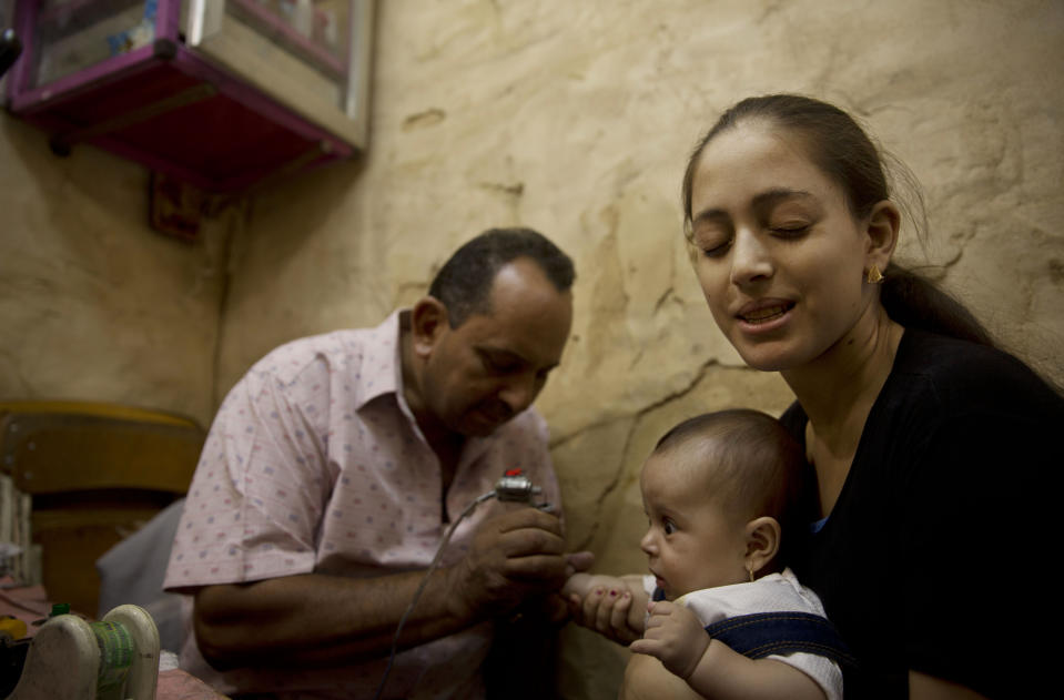 In this July 20, 2019, photo, a mother turns away as her daughter, Mariam, is tattooed with a small cross, a rite of passage for Coptic Christians, outside of St. Sama'ans Church in Cairo, Egypt. Egypt’s legal system grants the Coptic church full authority over personal status matters of Copts, namely marriage and divorce. But the church does not have the same powers over its followers’ inheritance rights. (AP Photo/Maya Alleruzzo)