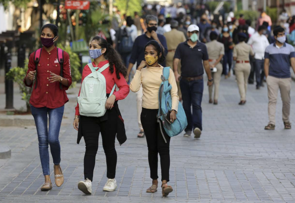 Crowd wearing masks walks through an outdoor area in India. 