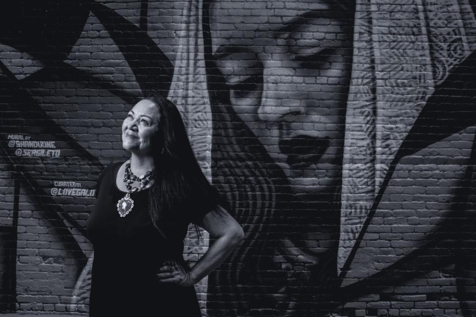 A woman stands in front of a painting on a brick wall