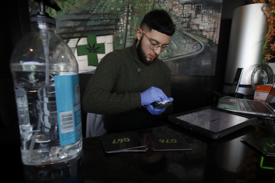 The Green Cross cannabis dispensary employee Sam, who did not want to give his last name, uses a disinfecting cleaning wipe on numbered cards that are handed to customers in San Francisco, Wednesday, March 18, 2020. As about 7 million people in the San Francisco Bay Area are under shelter-in-place orders, only allowed to leave their homes for crucial needs in an attempt to slow virus spread, marijuana stores remain open and are being considered "essential services." (AP Photo/Jeff Chiu)