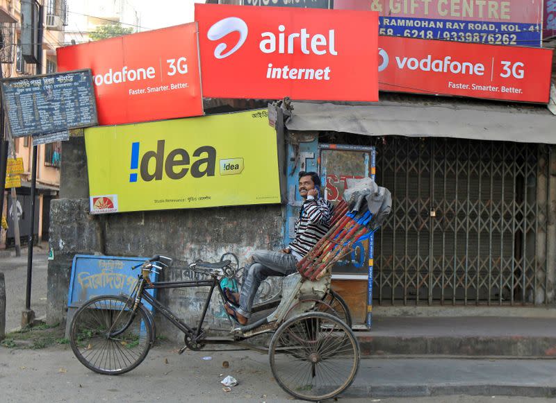 FILE PHOTO: A rickshaw puller speaks on his mobile phone as he waits for customers in front of advertisement billboards belonging to telecom companies in Kolkata