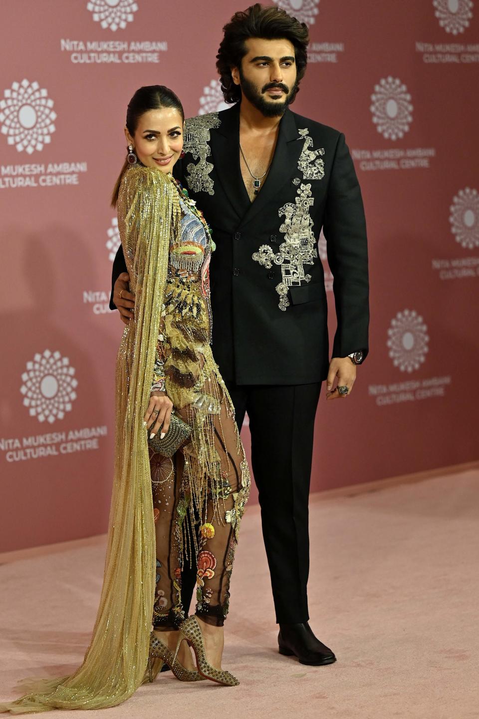 Bollywood actors Malaika Arora, left, and Arjun Kapoor strike a stylish pose, with Arora donning a flowy gold ensemble and Kapoor rocking a graphic black suit.