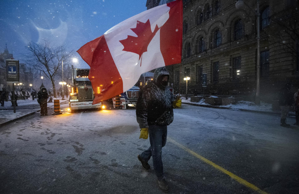 A protester carries a Canadian flag on Wellington Street across from Parliament Hill, during an ongoing protest against COVID-19 measures that has grown into a broader anti-government protest, in Ottawa, Ontario, on Thursday, Feb. 17, 2022. (Justin Tang/The Canadian Press via AP)