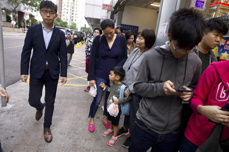 Pro-democracy activist Joshua Wong walks past people lined up to vote outside of a polling place in Hong Kong, Sunday, Nov. 24, 2019. Voting was underway Sunday in Hong Kong elections that have become a barometer of public support for anti-government protests now in their sixth month. (AP Photo/Ng Han Guan)