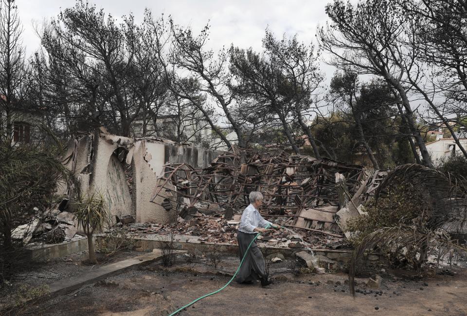 A woman sprays water outside her house that was damaged in the wildfires near the village of Neos Voutzas. Source: AP