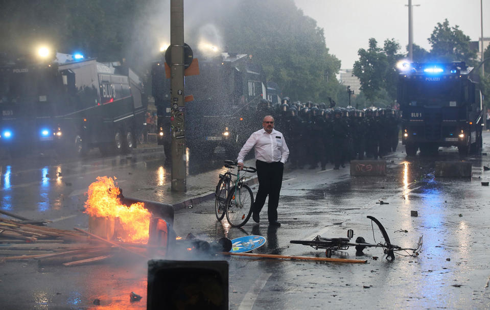 <p>A passerby walks his bike past burning waste bins and riot police using water cannon against protesters on July 7, 2017 in Hamburg, northern Germany, where leaders of the world’s top economies gather for a G20 summit. (Photo: Ronny Hartmann/AFP/Getty Images) </p>