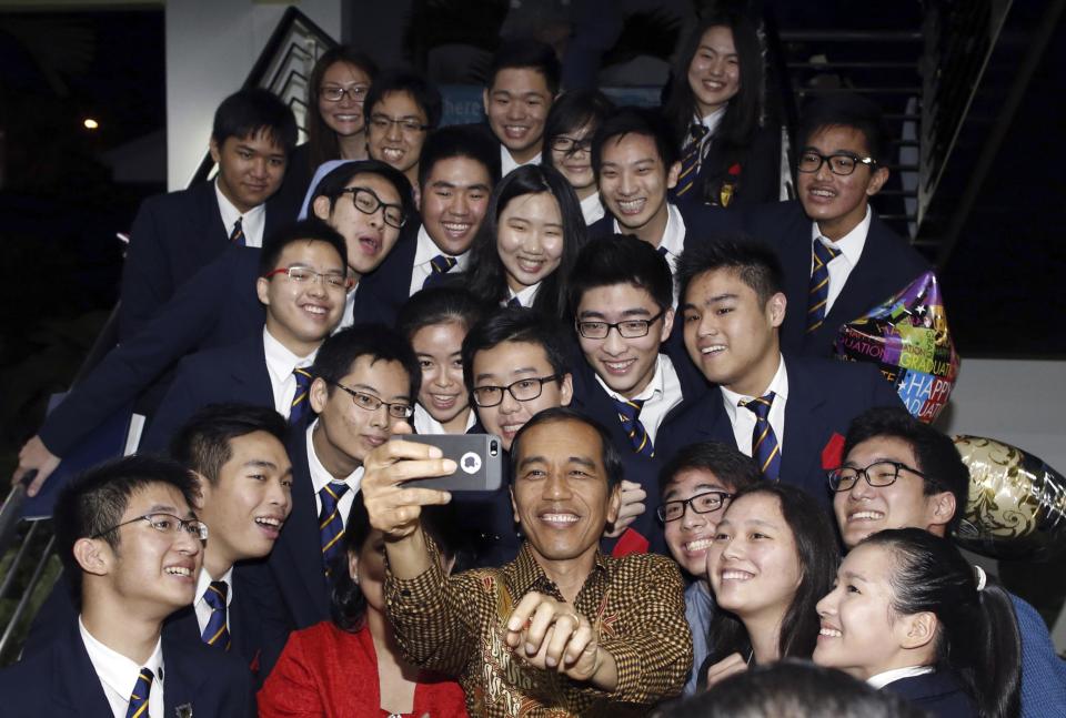 Indonesian President Joko "Jokowi" Widodo and his wife Iriana (in red) take a selfie with their son Kaesang Pangarep (holding balloon, 2nd R from top) and classmates after his graduation ceremony at Anglo-Chinese School (ACS) International in Singapore in this November 21, 2014 file photo. From flying economy class to making surprise visits to street markets and poor neighbourhoods, the leadership style of Widodo is proving very different to his predecessors, who were often seen as stiff and aloof. Widodo did not take the presidential plane to attend his son's university graduation ceremony in Singapore. Instead, he flew economy class on national carrier Garuda Airlines, winning praise on social media for his "humility". To match story INDONESIA-POLITICS/WIDODO REUTERS/Edgar Su/Files (SINGAPORE - Tags: EDUCATION POLITICS TPX IMAGES OF THE DAY)