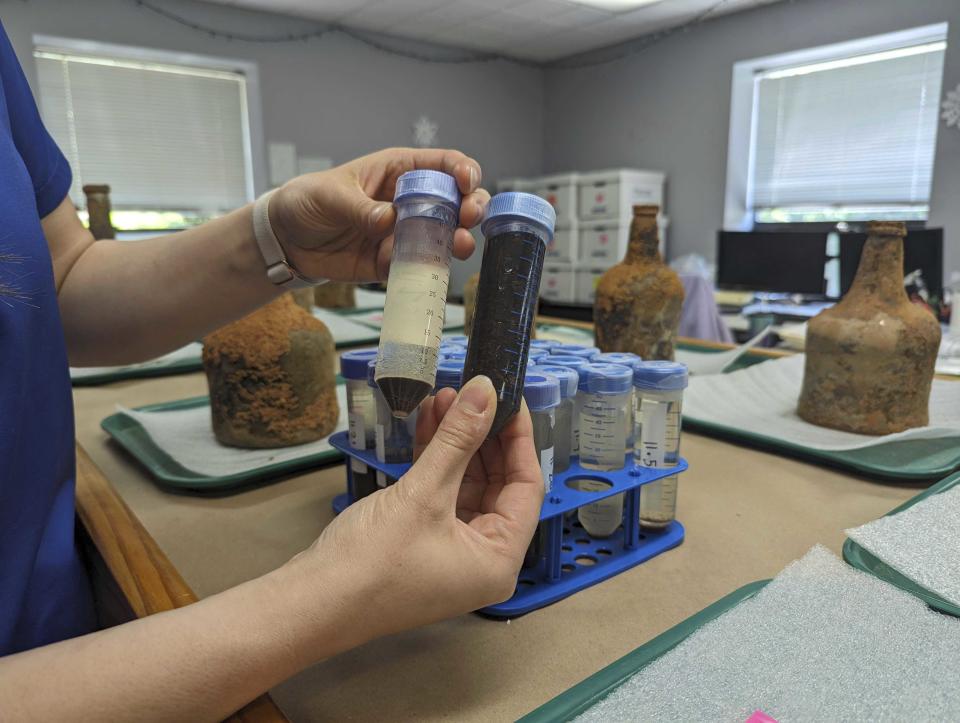 Curator Lily Carhart holds up different samples of liquid they extracted from a few dozen 18th-century glass bottles that contained fruit after they were unearthed from the cellar of George Washington's residence in Mount Vernon, Va., Monday, June 17, 2024. (AP Photo/Nathan Ellgren)