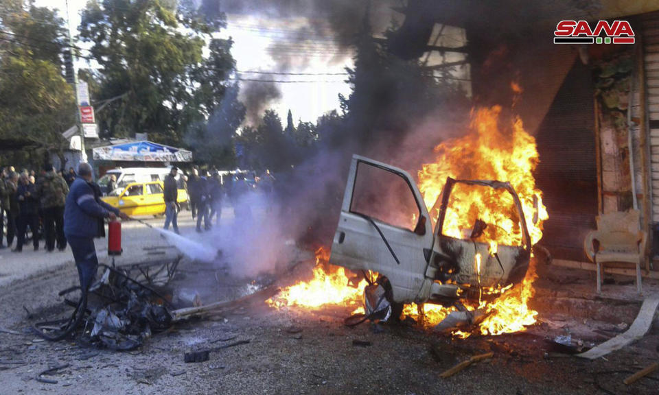 In this photo released by the Syrian official news agency SANA, a man tries to extinguishes flames rising from a burned car at the site of a deadly explosion, in the coastal city of Latakia, Syria, Tuesday, Jan. 22, 2019. Syrian state TV said Tuesday's blast was a car bomb that went off in Al-Hammam Square in Latakia that has been a government stronghold since the conflict began in March 2011. (SANA via AP)