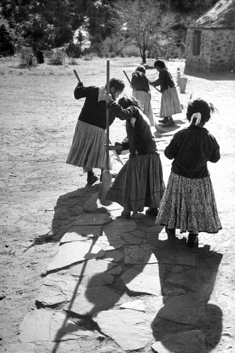 Navajo girls sweeping the sidewalk.