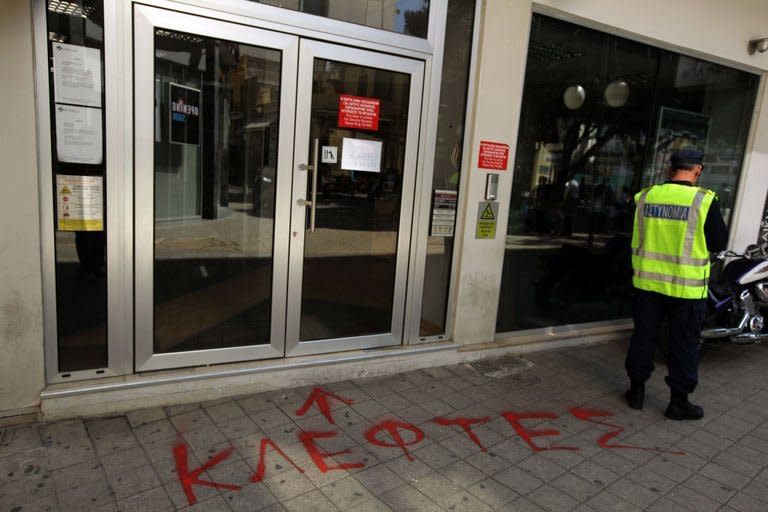 A Cypriot policeman stands next to graffiti in Greek reading "Thieves" at the entrance of closed branch of the Laiki (Popular) Bank in central Nicosia on March 20, 2013. The finance ministry said banks, which last opened their doors on Friday, will remain closed again on Thursday and Friday "on grounds of public interest in order to ensure financial stability."