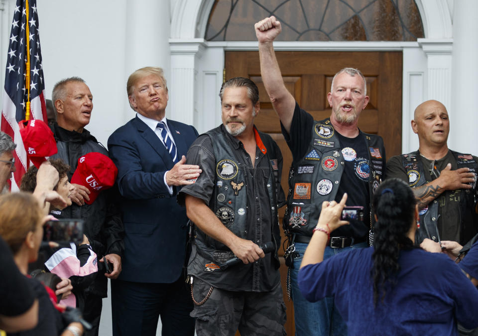 President Donald Trump stands in the rain with members of Bikers for Trump and supporters after saying the Pledge of Allegiance, Saturday, Aug. 11, 2018, at the clubhouse of Trump National Golf Club in Bedminster, N.J. (AP Photo/Carolyn Kaster)