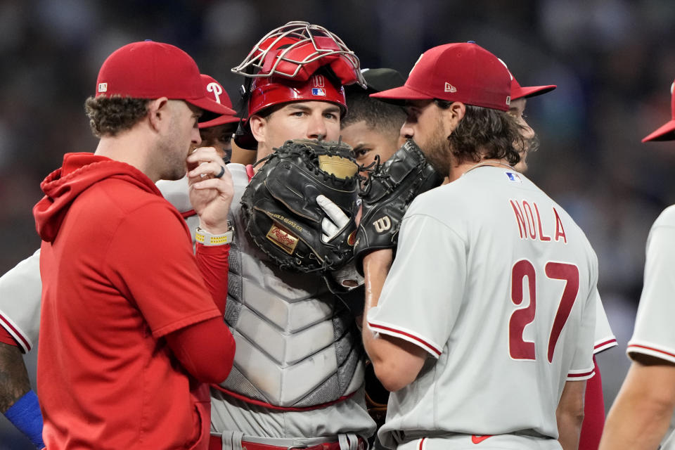 Philadelphia Phillies starting pitcher Aaron Nola (27) talks with pitching coach Caleb Cotham, left, and catcher J.T. Realmuto, center, during the third inning of a baseball game against the Miami Marlins, Sunday, July 9, 2023, in Miami. (AP Photo/Lynne Sladky)