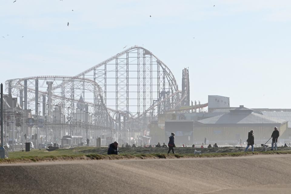 People enjoy the winter sunshine on the beach-front near the Blackpool Pleasure Beach amusement park in Blackpool, Lancashire on March 16, 2021, with the Big One roller coaster looming in the background. (Photo by Paul ELLIS / AFP) (Photo by PAUL ELLIS/AFP via Getty Images)