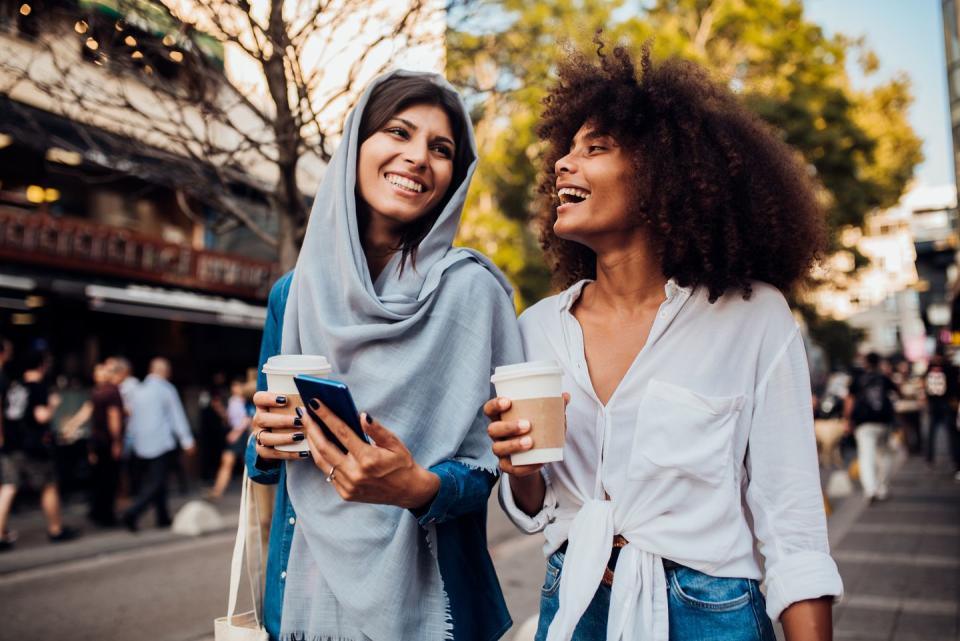 portrait of two young women drinking coffee whilst walking in the streets