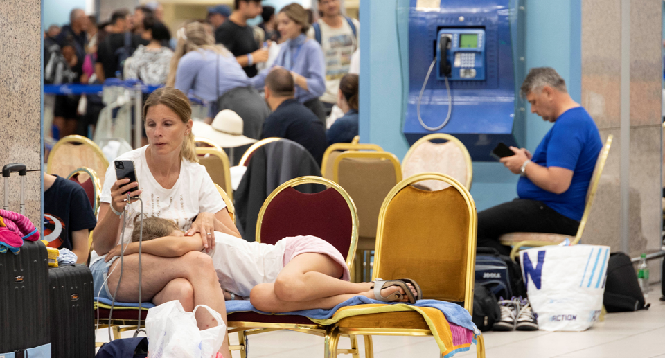 A woman checking her phone inside a crowded airport in Rhodes.