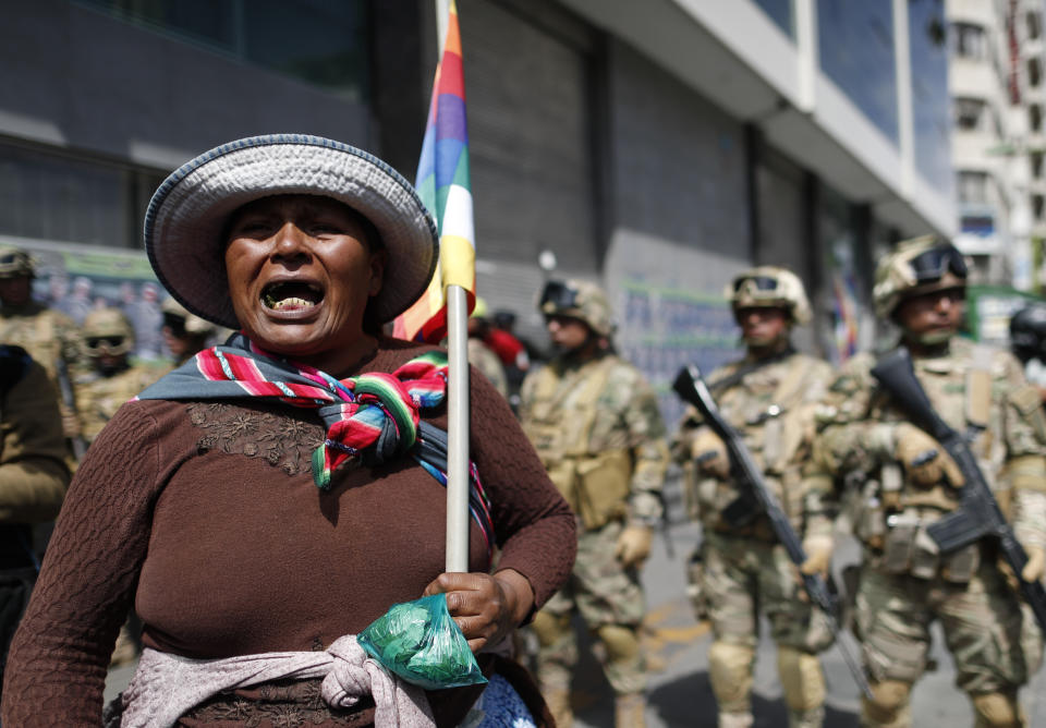 A backer of former President Evo Morales holds a Wiphala flag in front of soldiers blocking a street in downtown La Paz, Bolivia, Friday, Nov. 15, 2019. Bolivia's new interim president Jeanine Anez faces the challenge of stabilizing the nation and organizing national elections within three months at a time of political disputes that pushed Morales to fly off to self-exile in Mexico after 14 years in power. (AP Photo/Natacha Pisarenko)