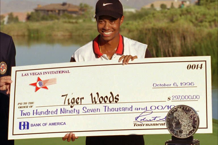 ARCHIVO - En esta fotografía de archivo del 6 de octubre de 1996, el golfista profesional novato Tiger Woods sonríe después de recibir un cheque y un trofeo por ganar el torneo de golf Las Vegas Invitational en el TPC en Summerlin en Las Vegas. Hace veinticinco años esta semana, Woods ganó por primera vez en el PGA Tour en el Las Vegas Invitational, cambiando el golf para siempre. (Foto AP / Lennox McLendon, archivo)