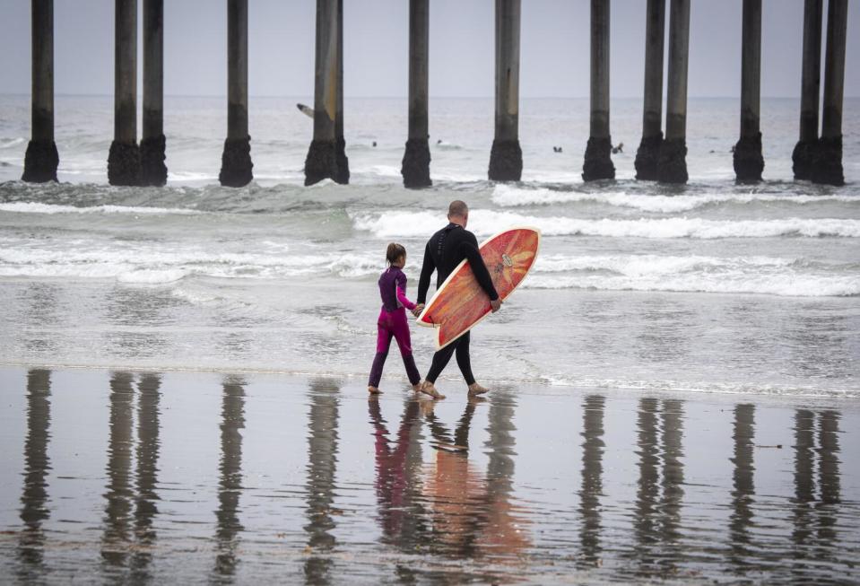 Beachgoers hold hands while heading out to surf