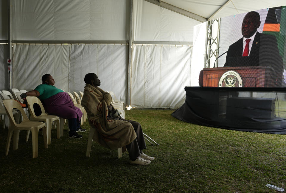 People listen to South African President Cyril President, right, through a screen, during Freedom Day celebrations in Pretoria, South Africa, Saturday April 27, 2024. The day marks April 27 when the country held pivotal first democratic election in 1994 that announced the official end of the racial segregation and oppression of apartheid. (AP Photo/Themba Hadebe)