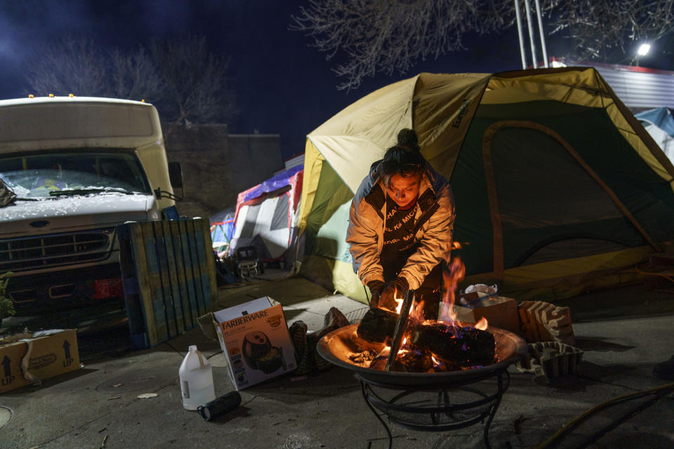 Amber Holmes pokes at a fire in the lot of an abandoned gas station where she lives in south Minneapolis along with dozens of other Native women in tents, Monday, Nov. 15, 2021. "When you're in addiction, you're just like this blazing fire," said the mother of four whose relatives are now raising her children. "It's so hard to put out." The painkillers she took for a kidney infection turned into a heroin addiction. She's been living outside for two years and started taking meth to avoid falling asleep and freezing to death. (AP Photo/David Goldman)