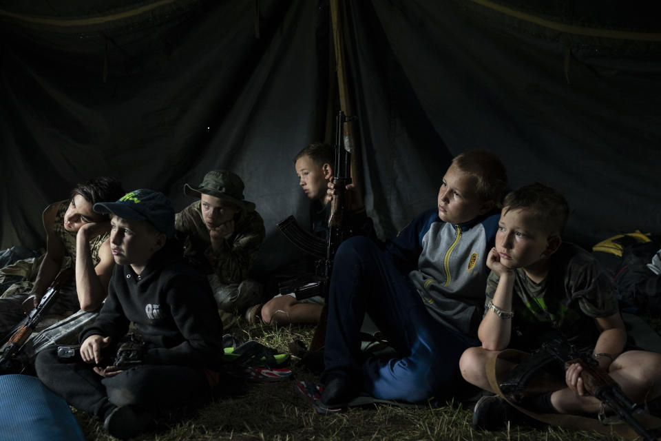 In this July 28, 2018 photo, young participants of the "Temper of will" summer camp, organized by the nationalist Svoboda party, sit inside a tent with their AK-47 riffles as they receive instructions during a tactical exercise in a village near Ternopil, Ukraine. The camp has two purposes: to train children to defend their country _ and to spread nationalist ideology. (AP Photo/Felipe Dana)