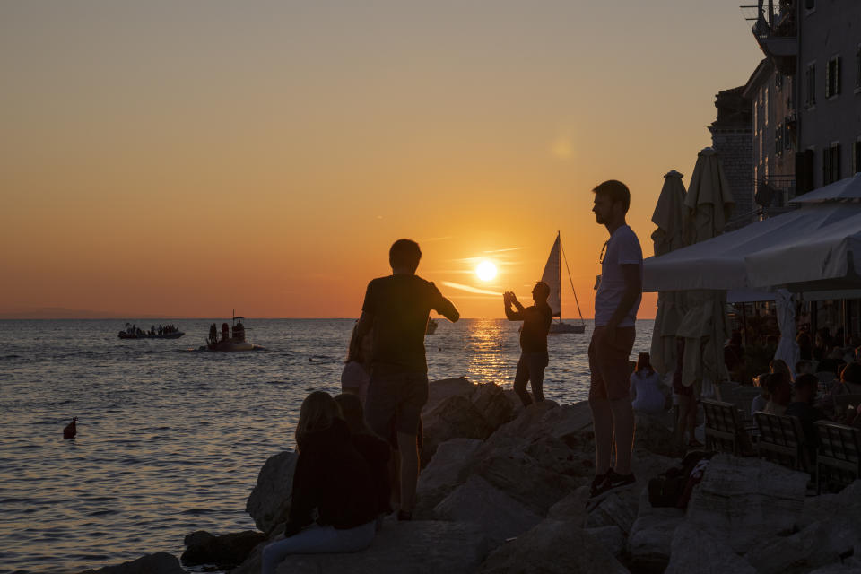 Holidaymakers enjoy the sunset on the seafront in the Adriatic town of Rovinj, Croatia, Friday, Aug. 27, 2021. Summer tourism has exceeded even the most optimistic expectations in Croatia this year. Beaches along the country's Adriatic Sea coastline are swarming with people. Guided tours are fully booked, restaurants are packed and sailboats were chartered well in advance. (AP Photo/Darko Bandic)