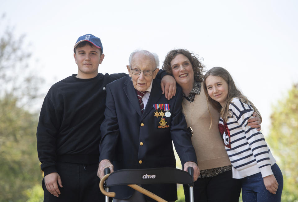 FILE - In this April 16, 2020 file photo, 99-year-old war veteran Captain Tom Moore, with from left, his grandson Benji, daughter Hannah Ingram-Moore and granddaughter Georgia, at his home in Marston Moretaine, England, after he achieved his goal of 100 laps of his garden. The legacy of Capt. Tom Moore, the super fundraiser who died Tuesday, Feb. 2, 2021 of COVID-19, lives on in Imogen Papworth-Heidel — and many others. The 11-year-old soccer player, who dreams of playing for England, watched Capt. Tom pushing his walker up and down his garden to raise money for the National Health Service. So she decided to help by doing something she’s good at: keepy uppies — kicking the ball into the air and passing it from one foot to the other without letting it touch the ground. Imogen was able to raise 15,000 pounds ($20,500) for key workers. Similar fundraising feats have been performed by a 5-year-old amputee and a 90-year-old woman in the Scottish Highland. (Joe Giddens/PA via AP, File)