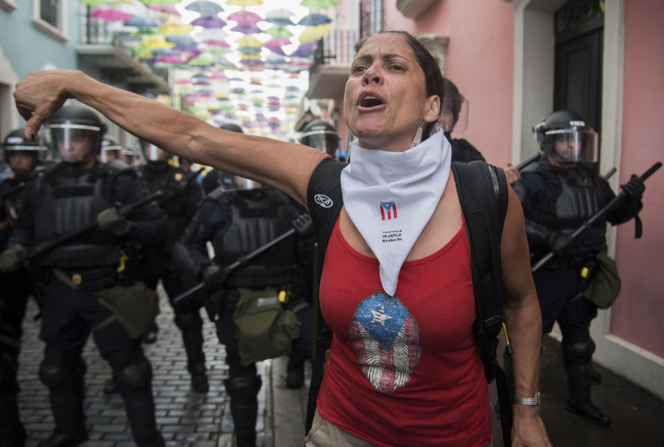 A woman gives a thumbs down where police block demonstrators from advancing to La Fortaleza governor's residence in San Juan, Puerto Rico, Sunday, July 14, 2019. Protesters are demanding Gov. Ricardo Rosselló step down for his involvement in a private chat in which he used profanities to describe an ex-New York City councilwoman and a federal control board overseeing the island's finance. (AP Photo/Carlos Giusti)