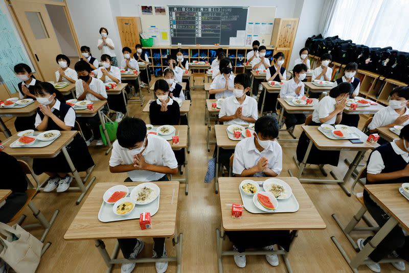 Students gesture before they start taking school lunch at Senju Aoba Junior High School in Tokyo