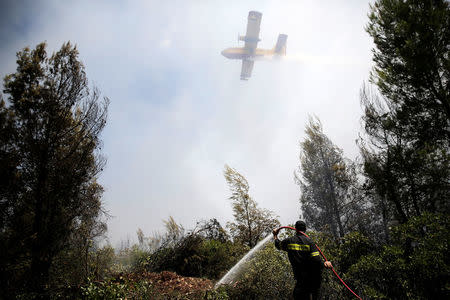 A firefighter operates as an airplane flies over during a wildfire near the village of Kalamos, north of Athens, Greece, August 14, 2017. REUTERS/Costas Baltas