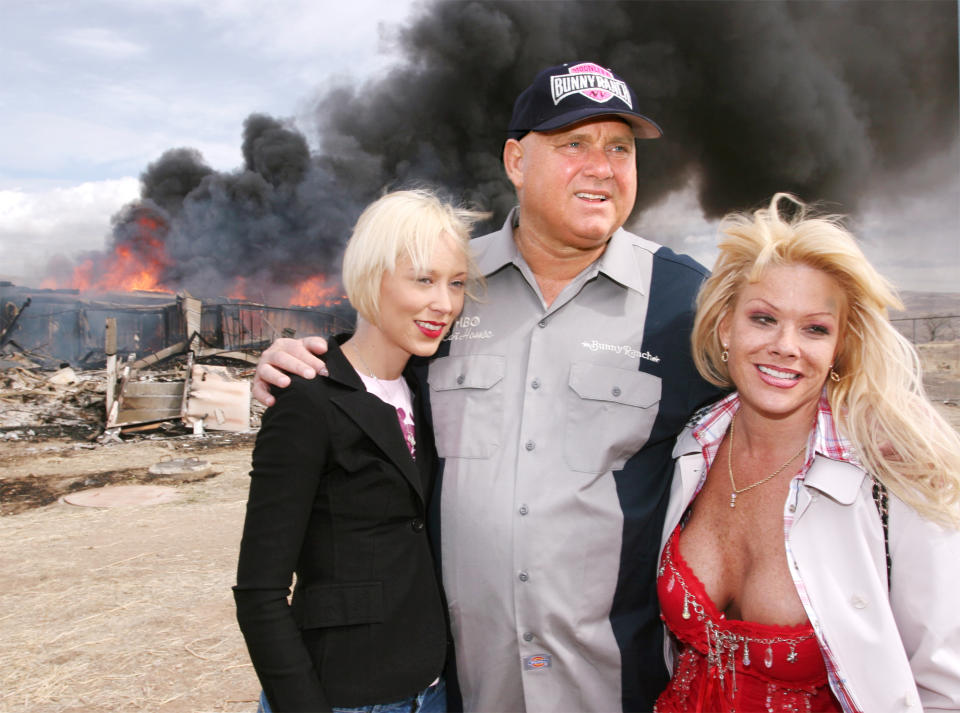 FILE - In this March 25, 2007, file photo, Moonlite Bunnyranch brothel owner Dennis Hof poses with two of his "working girls" Brooke Taylor, left, and a woman working under the name "Airforce Amy", right, as firefighters burn down remains of the former Mustang Ranch 2 brothel east of Reno, Nev. Hof, a legal pimp who has fashioned himself as a Donald Trump-style Republican candidate has died, Nevada authorities said Tuesday, Oct. 16, 2018. (AP Photo/Debra Reid, file)