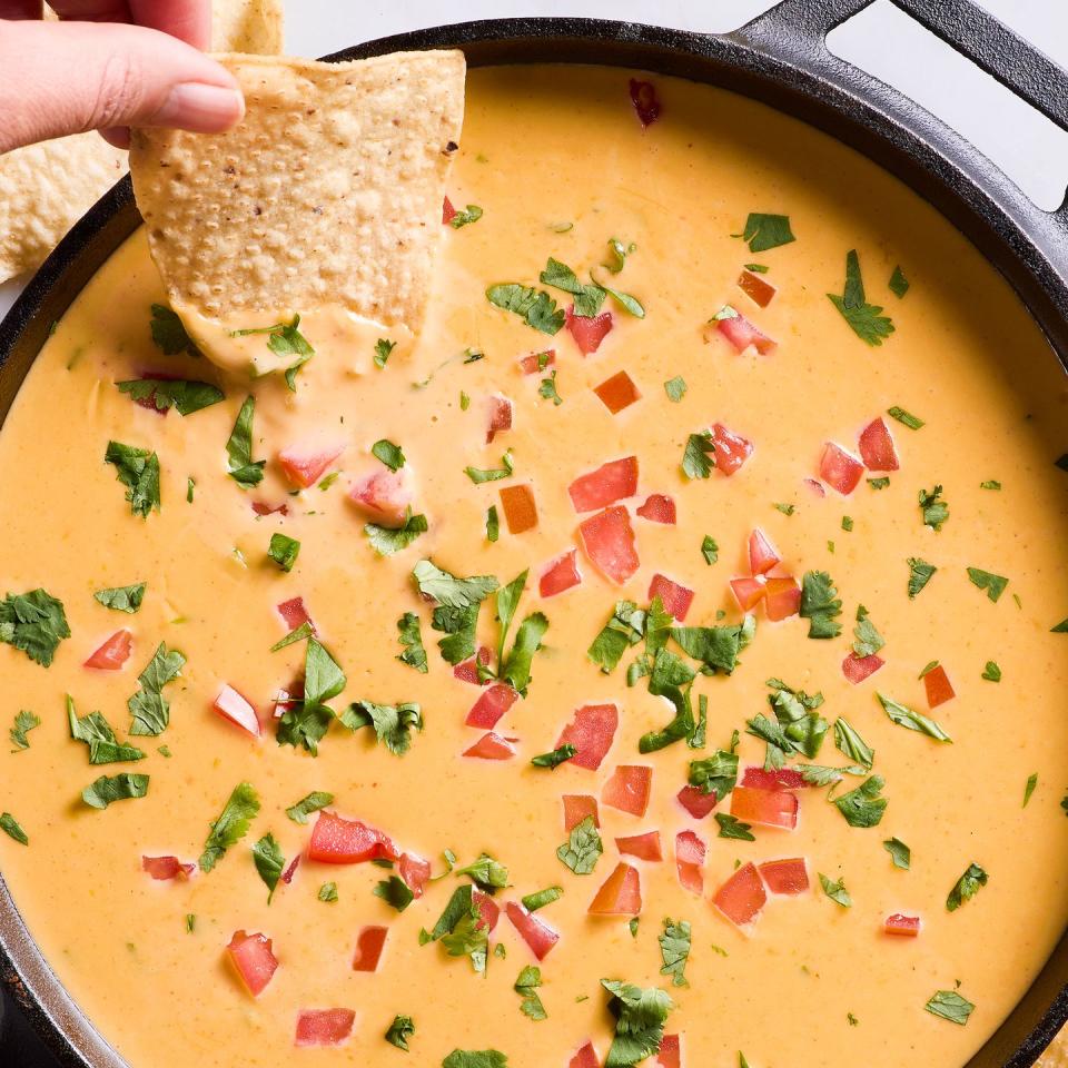 queso topped with tomatoes and cilantro in a black cast iron skillet