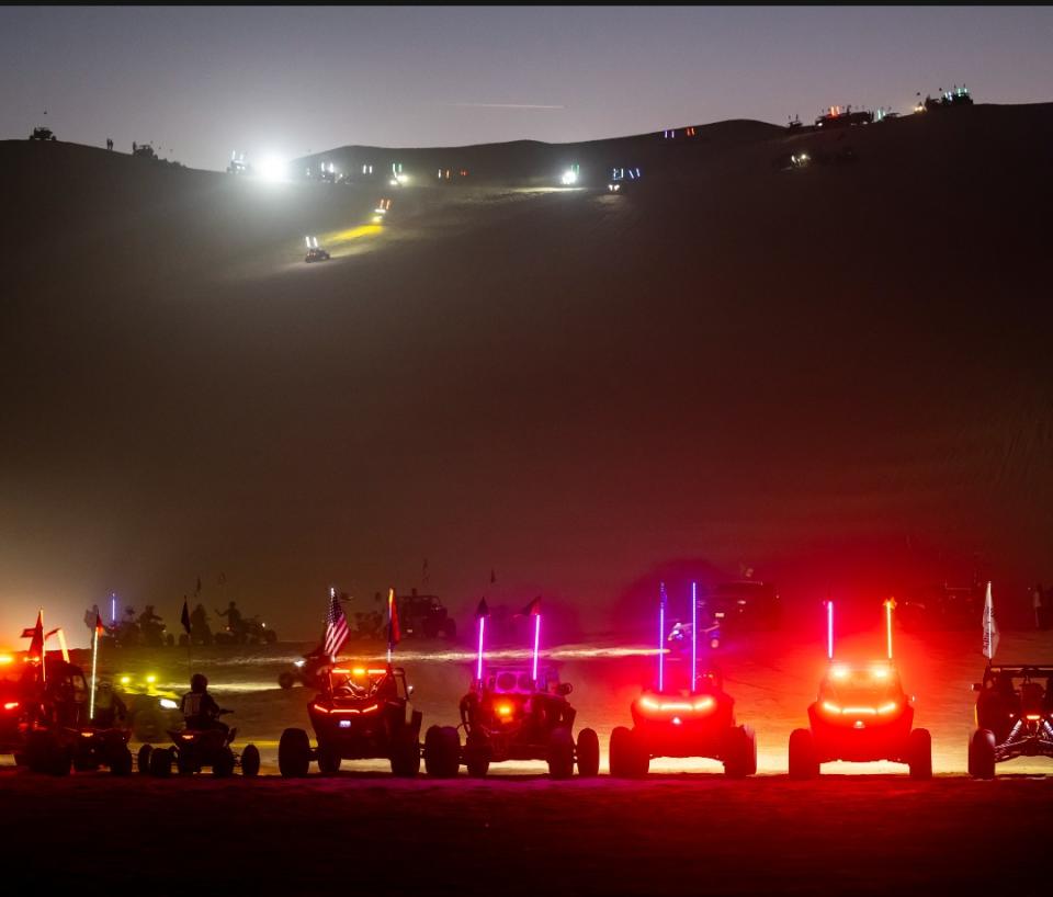 Lit vehicles cruising on the sandy slopes of Oldsmobile Hill at night.
