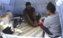 Daniel Ejube, left, and Enjei Grace, from Cameroon, sit inside a tent they have been living in for nearly five months inside a section of a United Nations controlled buffer zone that cuts across ethnically divided Cyprus' capital Nicosia on Wednesday, Oct. 20, 2021. Grace and Ejube have been stuck in a legal limbo inside the buffer zone that separates Cyprus' breakaway north from the internationally recognized south. The U.N. refugee agency says Grace and Ejube should be allowed to apply for asylum in the south. (AP Photo/Philippos Christou)